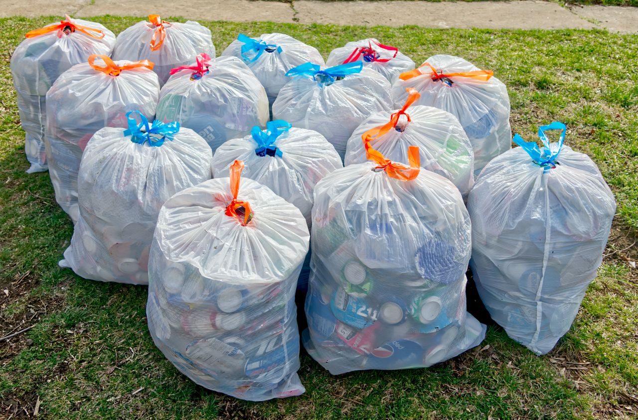 Plastic trash bags filled with recyclable materials on grass, raising recycling awareness.